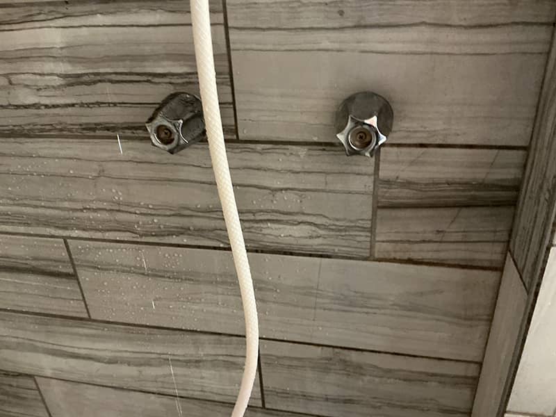 Older two-handle shower valve in tile before repair and replacement
