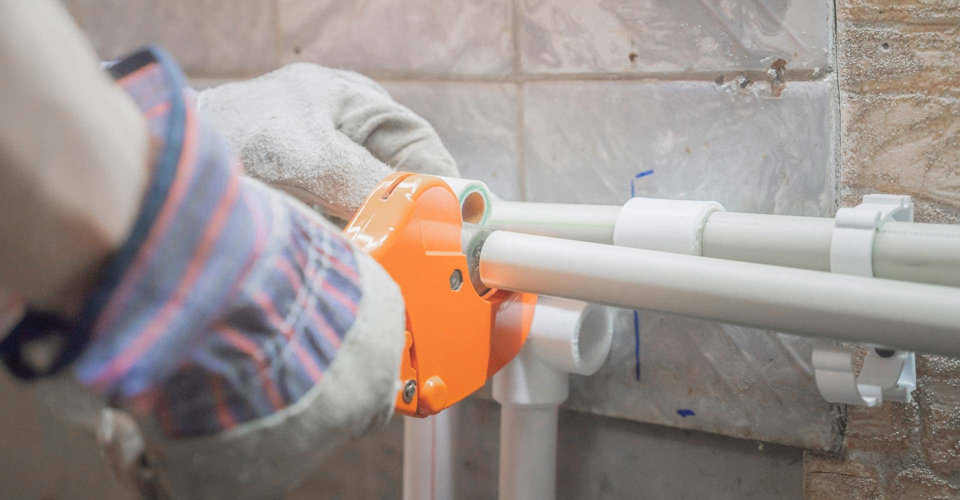 gloved hands cutting white plastic pipe with an orange pipe cutter